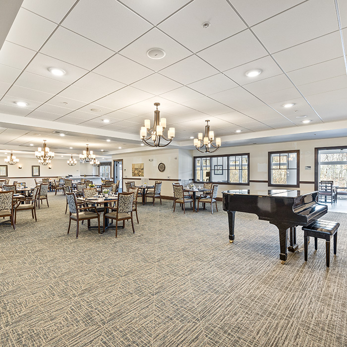 Dining room with tables, arm chairs and a grand piano.