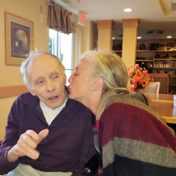 Monica leans over to give her dad a kiss on the cheek at McKenna Crossing senior living community.