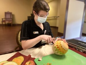 Madelyn carves intricate pattern into cantaloupe. 