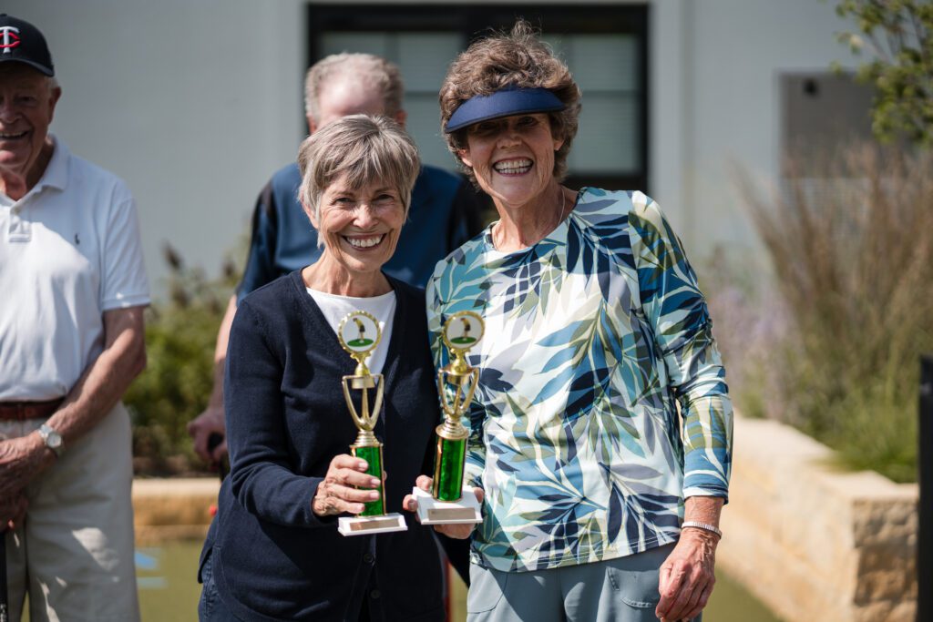 Smiling older women pose with golf trophies.