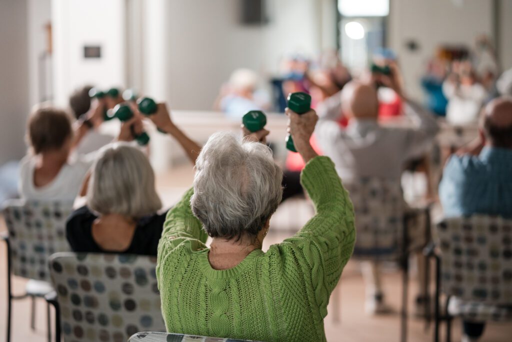 Older adults participate with weights in a seated fitness class.